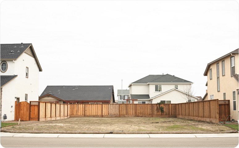 A fenced empty lot between two homes.