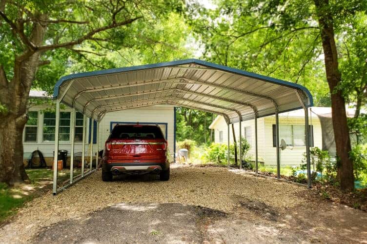 A carport surrounded by trees and a red car inside of it.