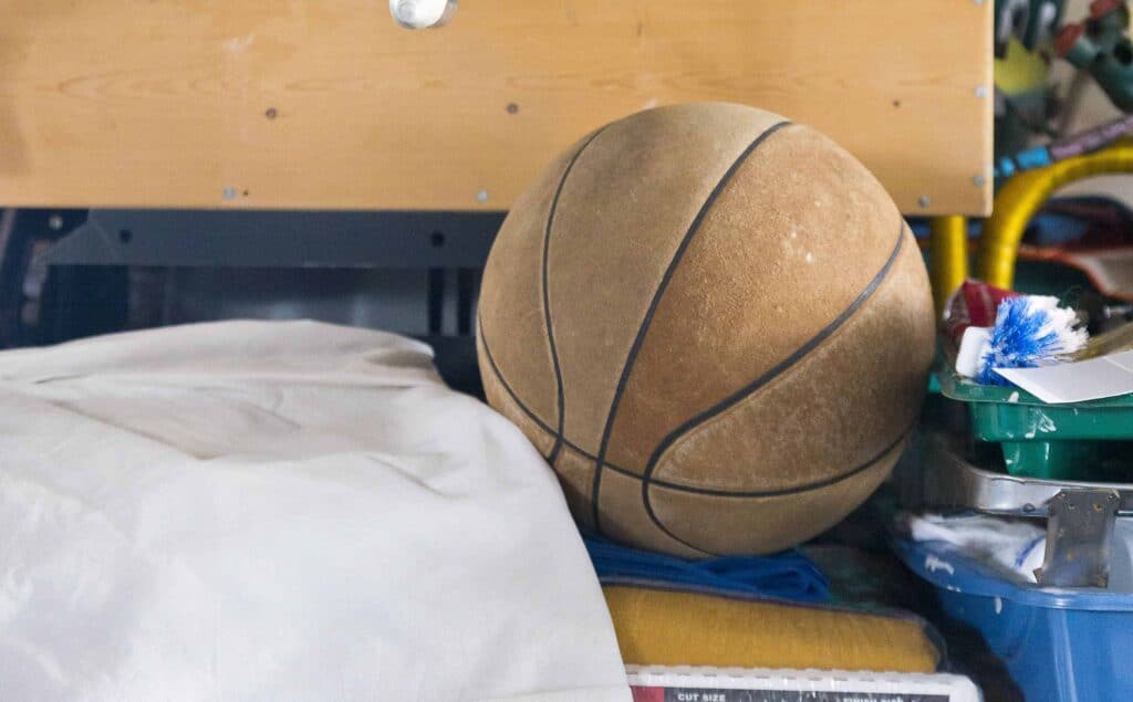 A worn basketball resting on a bench in a cluttered garage.