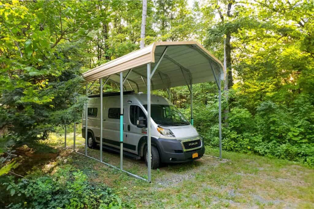 A carport on grass surrounded by trees and bushes.