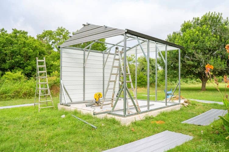 A small garage under construction with tools and ladder inside of it.