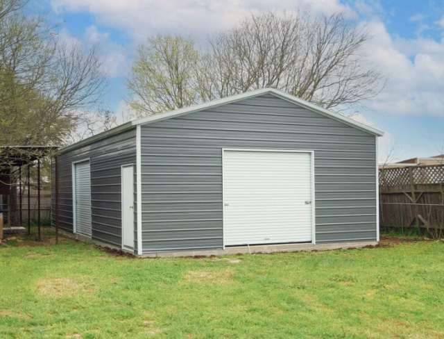 Gray metal garage with a garage door on front and walk in door and garage door on the side.