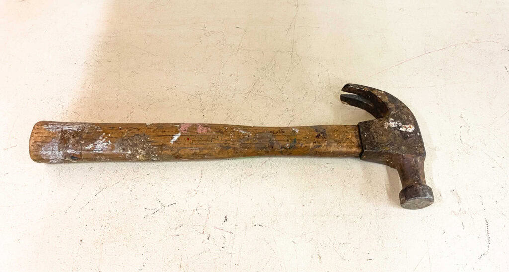 A well-used hammer with a wooden handle lying on a garage floor.