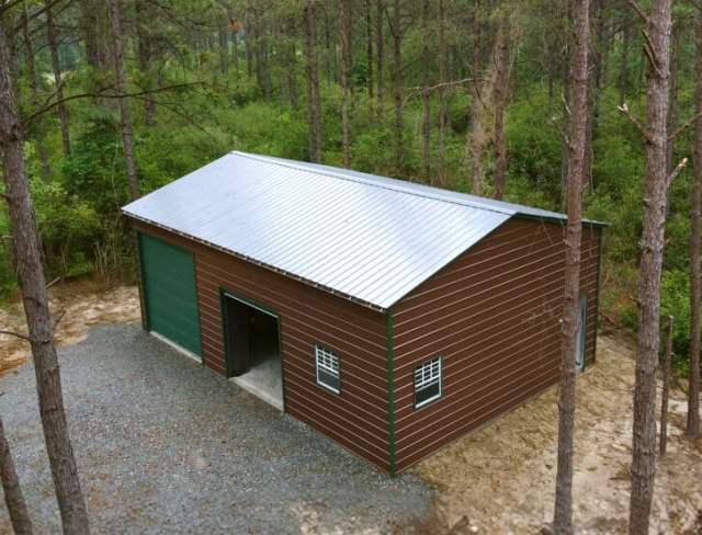 Large brown garage with green garage doors in a forest.