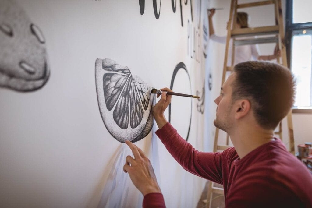 man painting a mural on a white garage wall