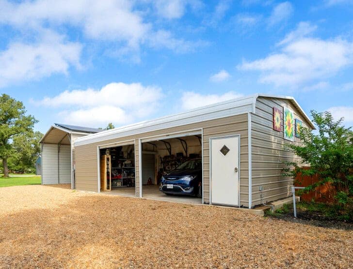 A large garage with two garage doors and a car inside it. Next to the garage is a carport.