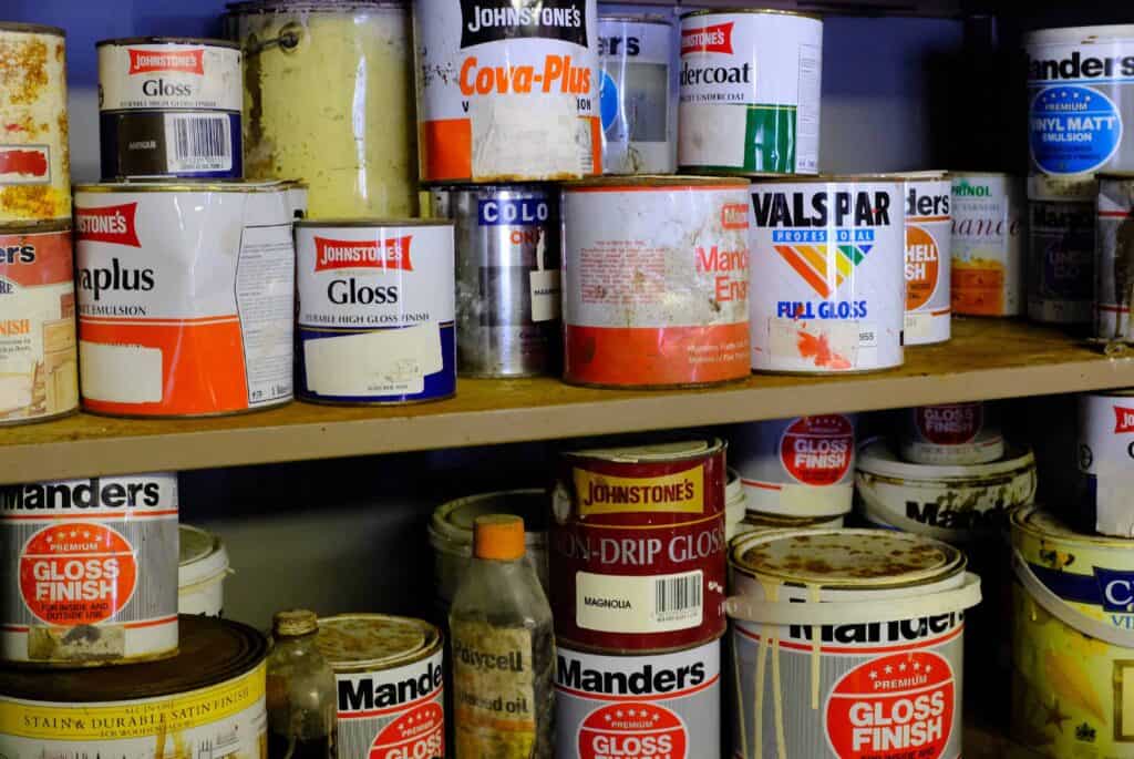 Old and partially used paint cans stored on a shelf in a garage.