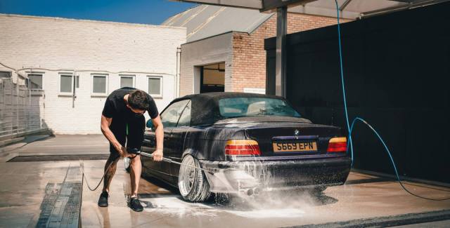 Man pressure washing a car at an outdoor car wash station