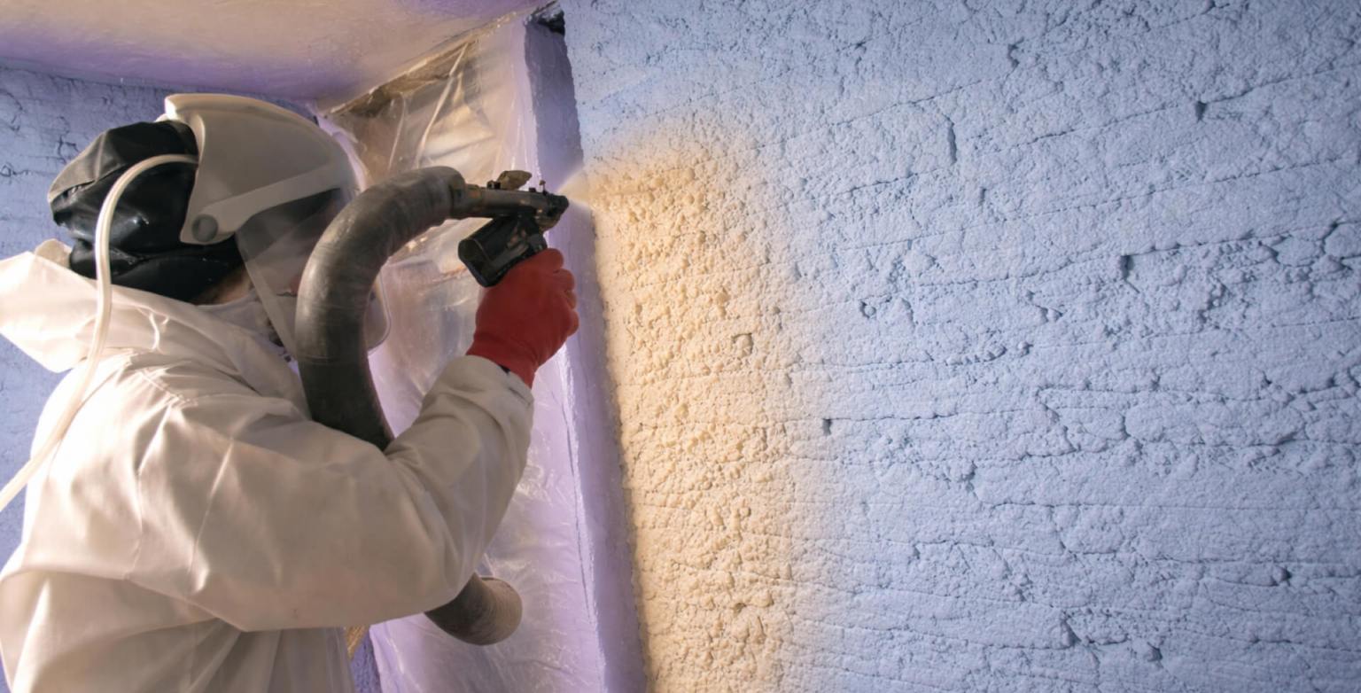 A worker in a hazmat suit applying a purple spray foam insulation on a wall