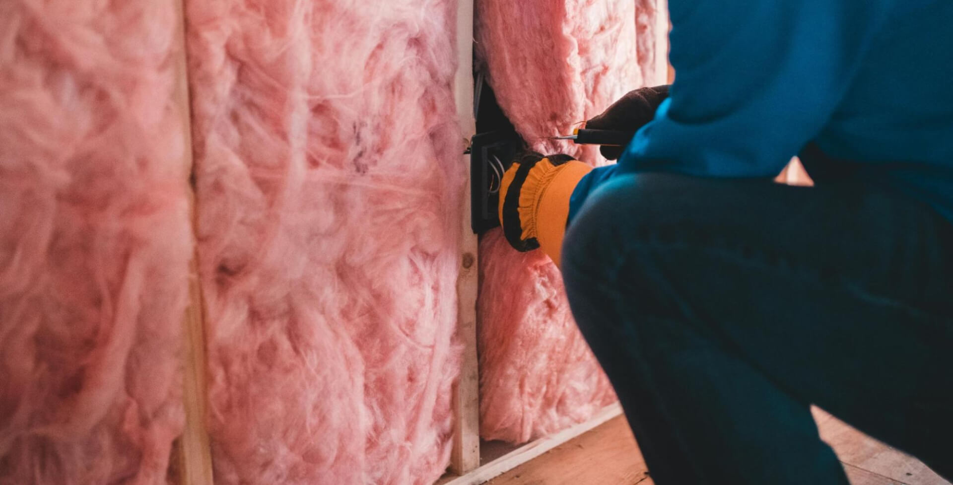 A worker installing fiberglass insulation on a wall
