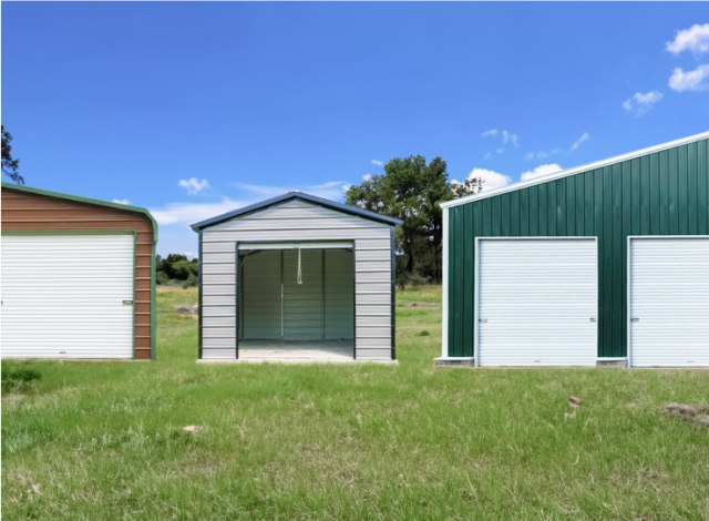 Three metal buildings standing in a grassy field under a clear blue sky