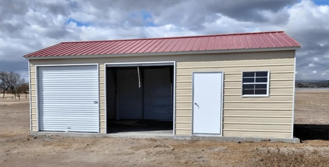 Metal garage with a red roof and roll-up door in an open landscape