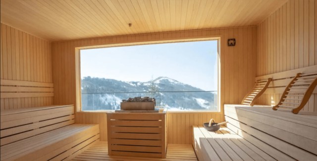 Sauna with wooden interiors and a large window overlooking snowy mountains