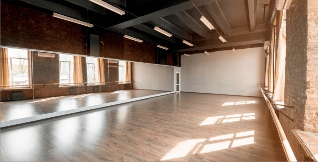 Spacious dance studio with brick walls, large mirrors, and wooden flooring