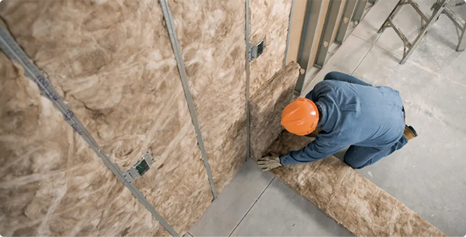 A worker installing fiberglass insulation on a wall