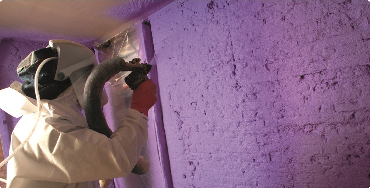 A worker in a hazmat suit applying a purple spray foam insulation on a wall