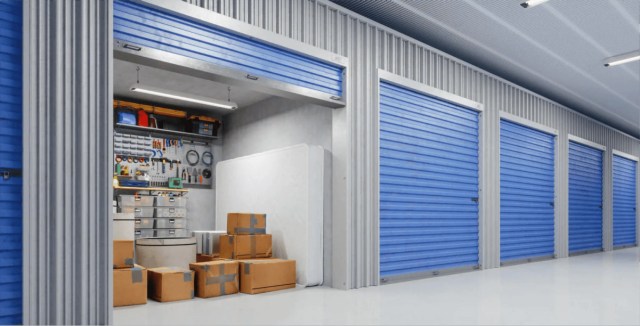 Storage unit with a partially open blue roll-up door, revealing packed boxes, tools, and shelves inside