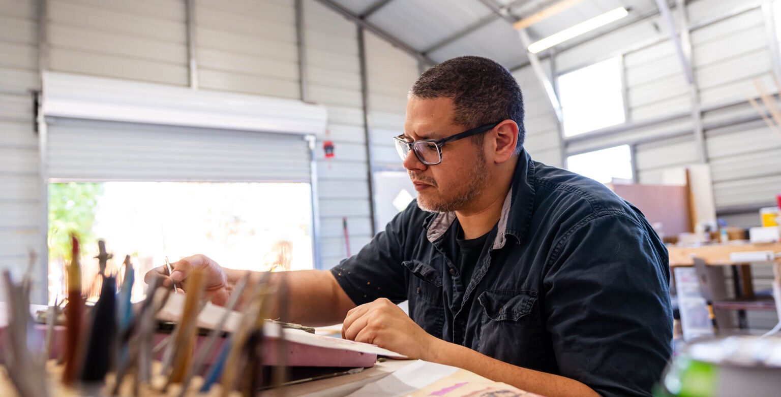 Sculptor Yousif working on artwork at his workbench inside his 20×20 metal garage studio in Austin, Texas