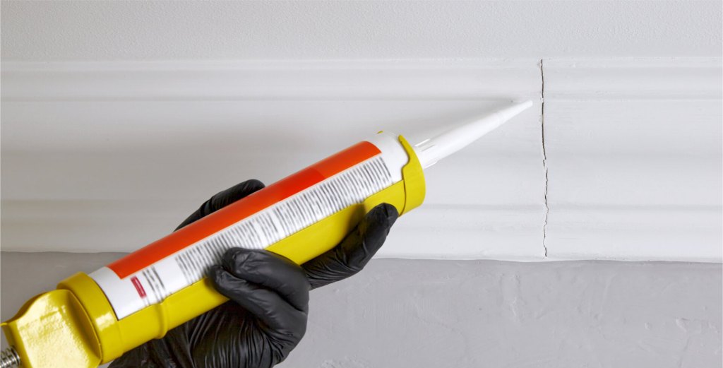 Hand applying caulk to a crack in white crown molding