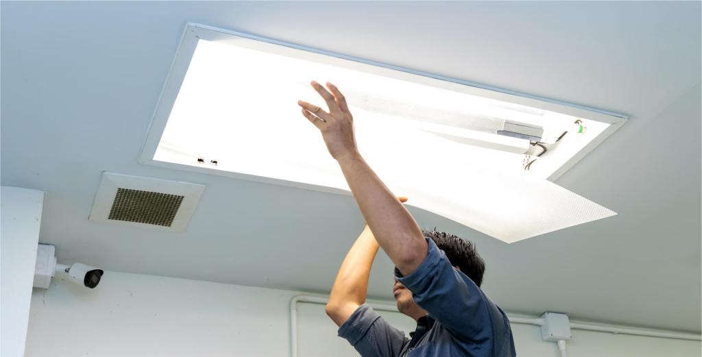 Worker installing a ceiling light panel in a commercial space