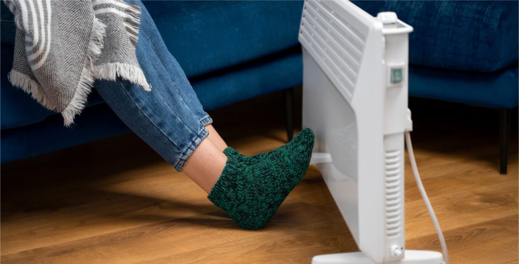 Person wearing warm socks resting feet near an electric heater