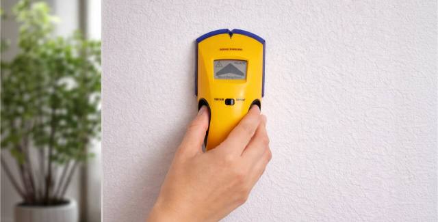Magnetic stud finder being used on an interior wall to locate wall studs