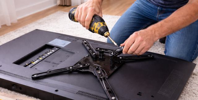 Person attaching a TV wall mount bracket to the back of a flat-screen television
