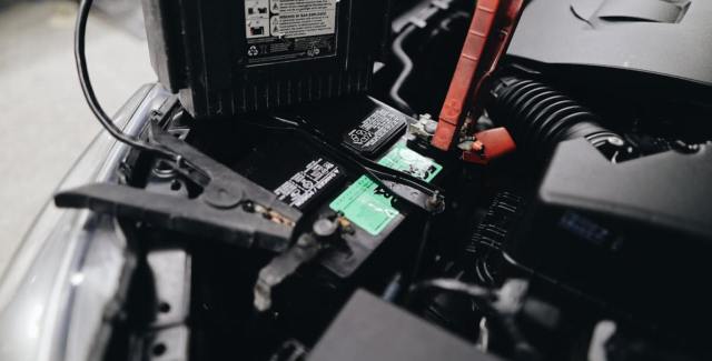 Close-up of a car battery being jump-started with jumper cables in an engine compartment