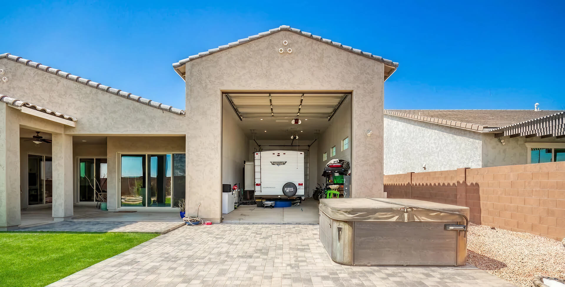 Modern home with open garage containing RV trailer and outdoor patio