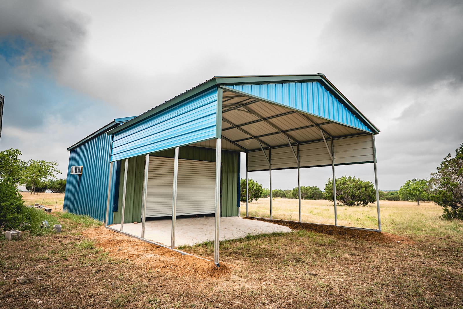 A blue and green metal carport with a vertical roof attached to a matching enclosed metal garage.