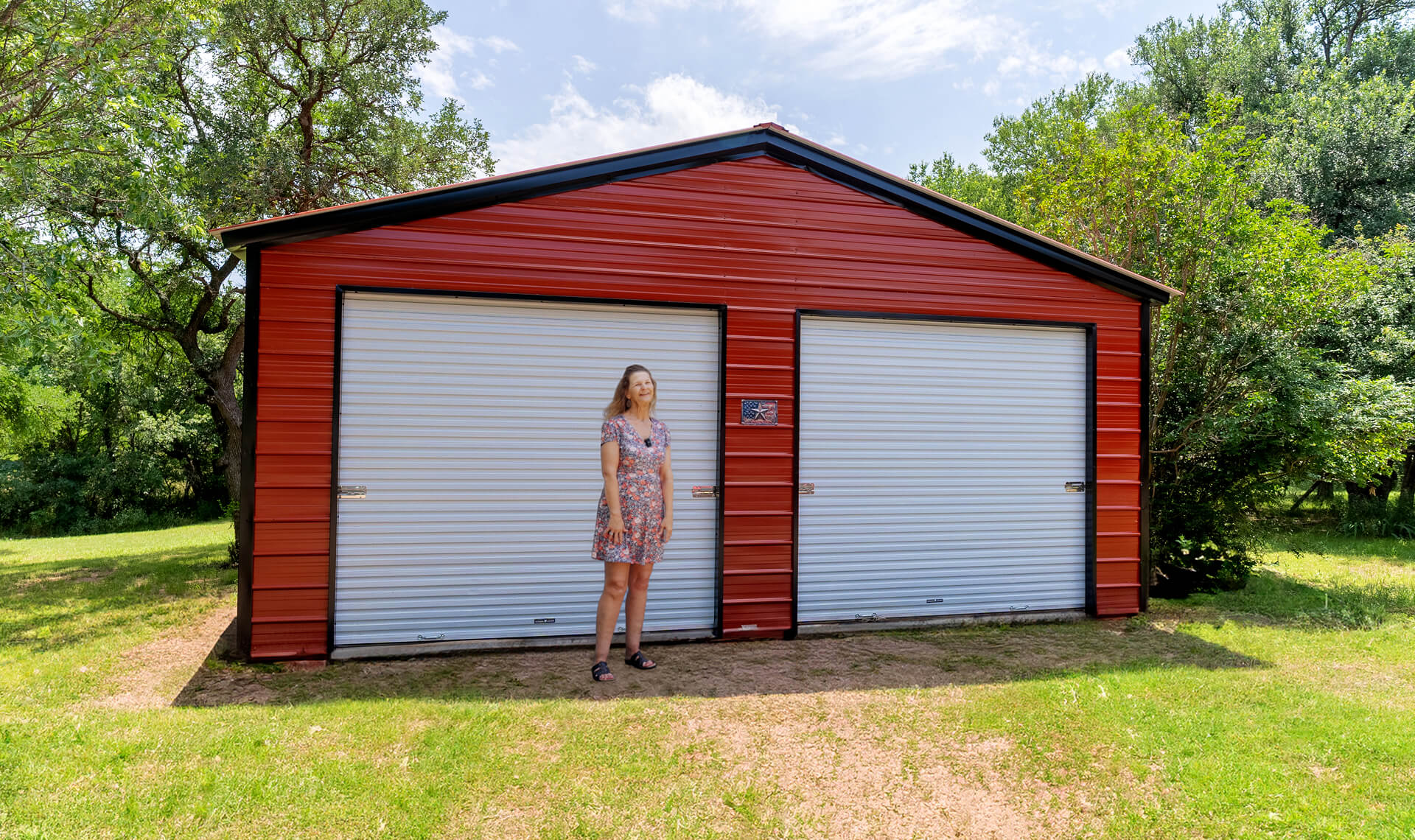 Custom red metal garage building with dual roll-up doors on a residential property, featuring durable steel siding, spacious storage capacity, and modern prefab workshop design.