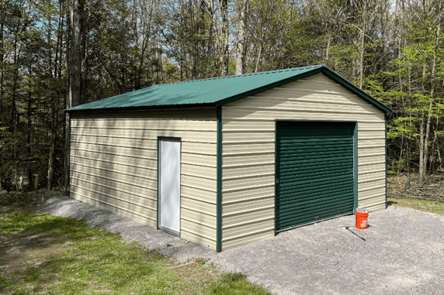 Prefab metal garage building with green roof and roll-up garage door, used for equipment storage, vehicle protection, and backyard workshop space.