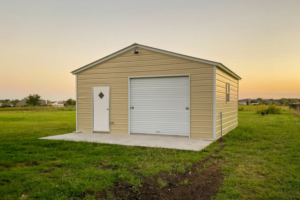 Compact beige metal barn installed on a concrete slab in a grassy residential setting, featuring a roll-up garage door and side entry, ideal for hobby farm storage, small equipment, or a multi-use workspace within a manageable footprint.