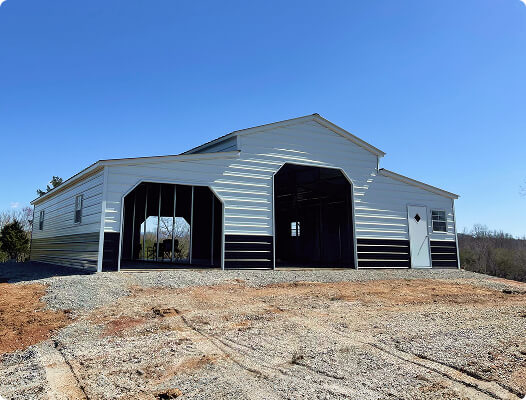 Large white and black barn-style metal garage with two open bays and a walk-in door on a gravel lot
