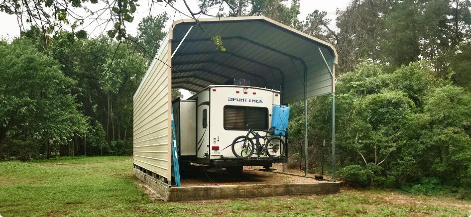 Enclosed metal carport sheltering a camper RV in a wooded backyard