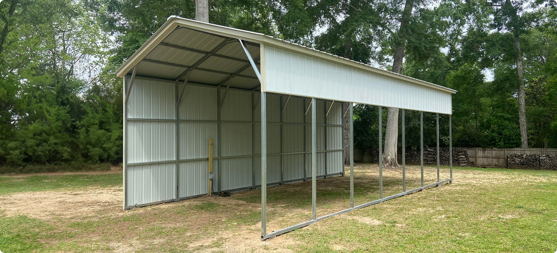 Enclosed metal carport with side panels in a wooded backyard