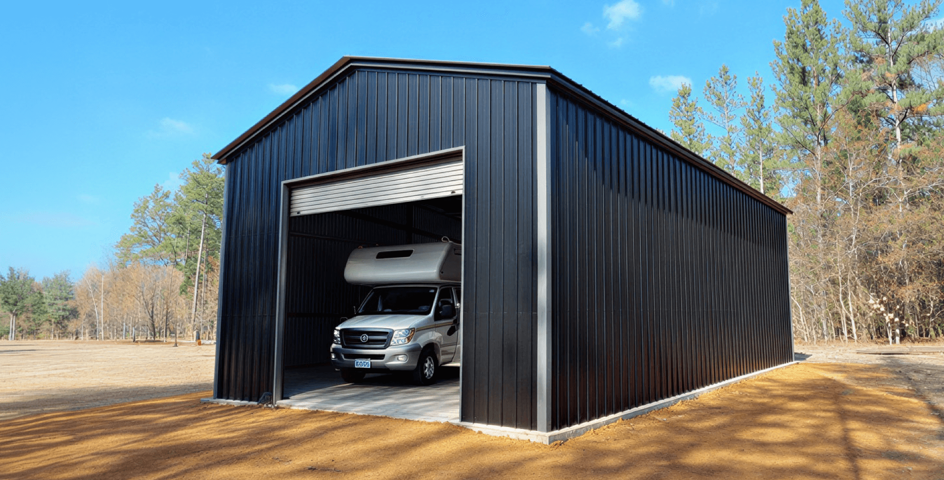 Black vertical metal RV garage with large roll-up door and concrete slab foundation, housing a white motorhome inside for secure weather-resistant RV storage.