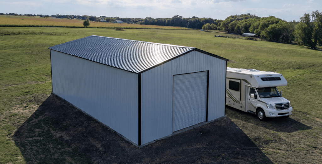 Large white metal RV garage with vertical siding, black trim, and roll-up door, positioned on a spacious rural property with a motorhome parked beside it for secure RV storage.