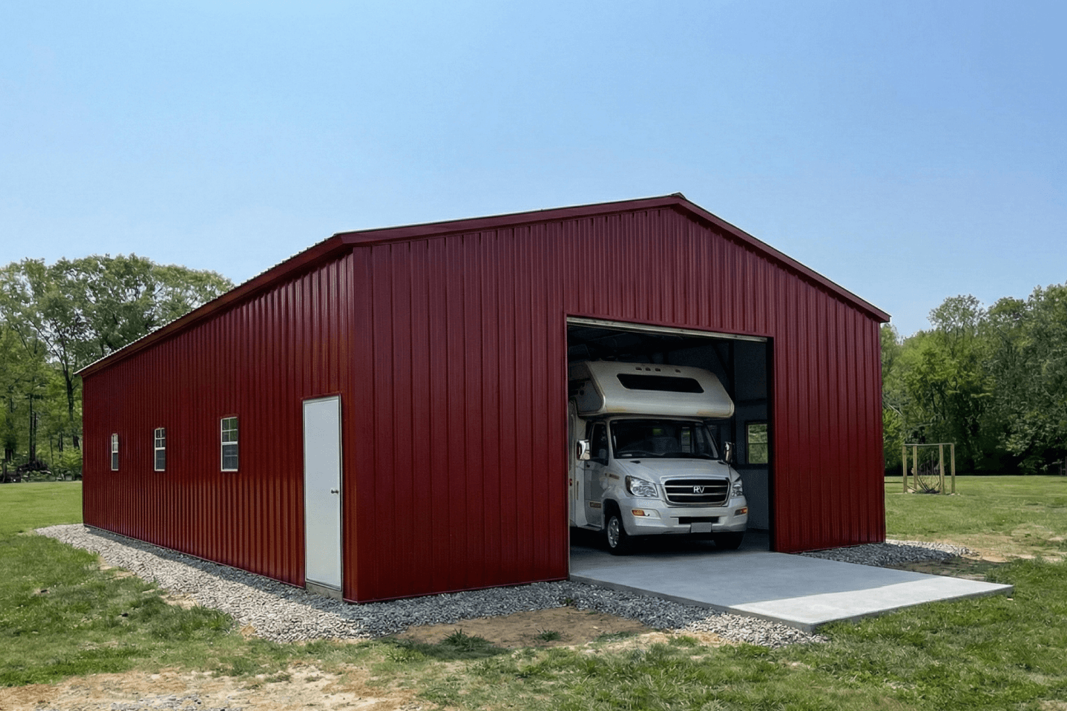 Red vertical metal RV garage with large open roll-up door and side entry door, featuring a white camper stored inside on a concrete slab, ideal for motorhome storage and weather protection.
