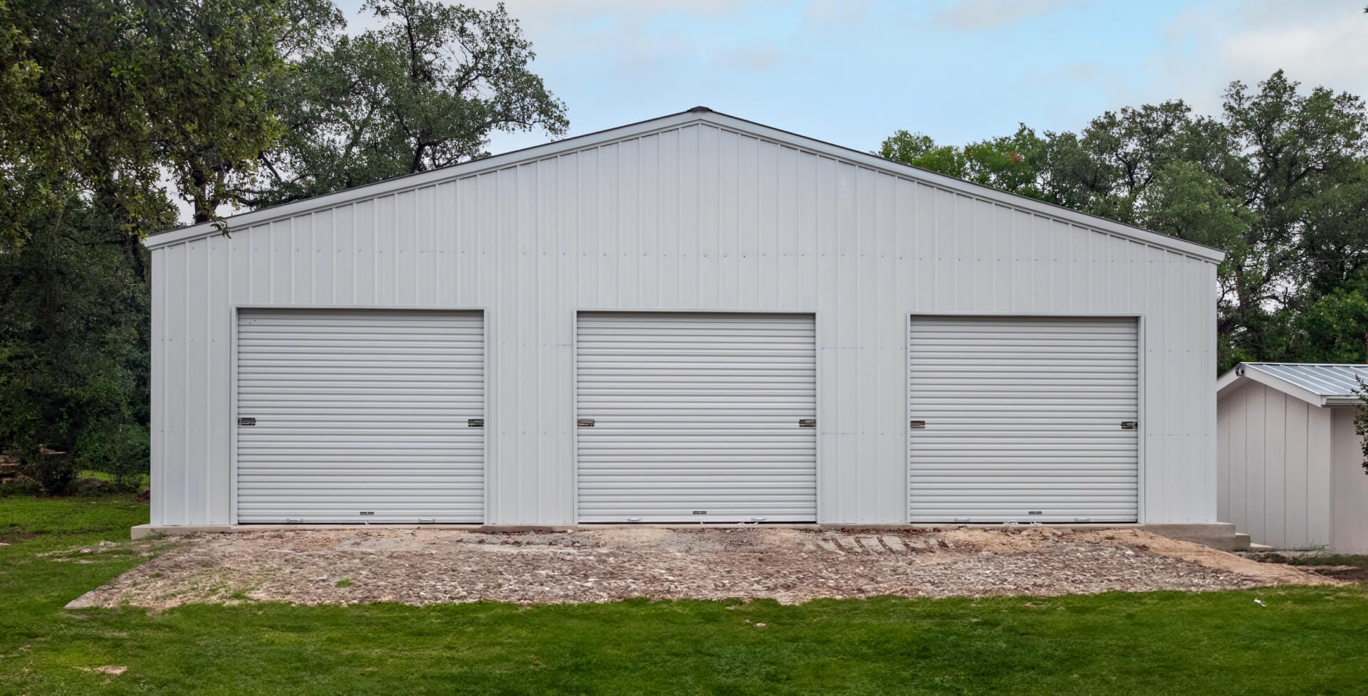 White three-car metal garage with roll-up doors and vertical siding, built on a concrete slab for residential storage and multi-vehicle parking.