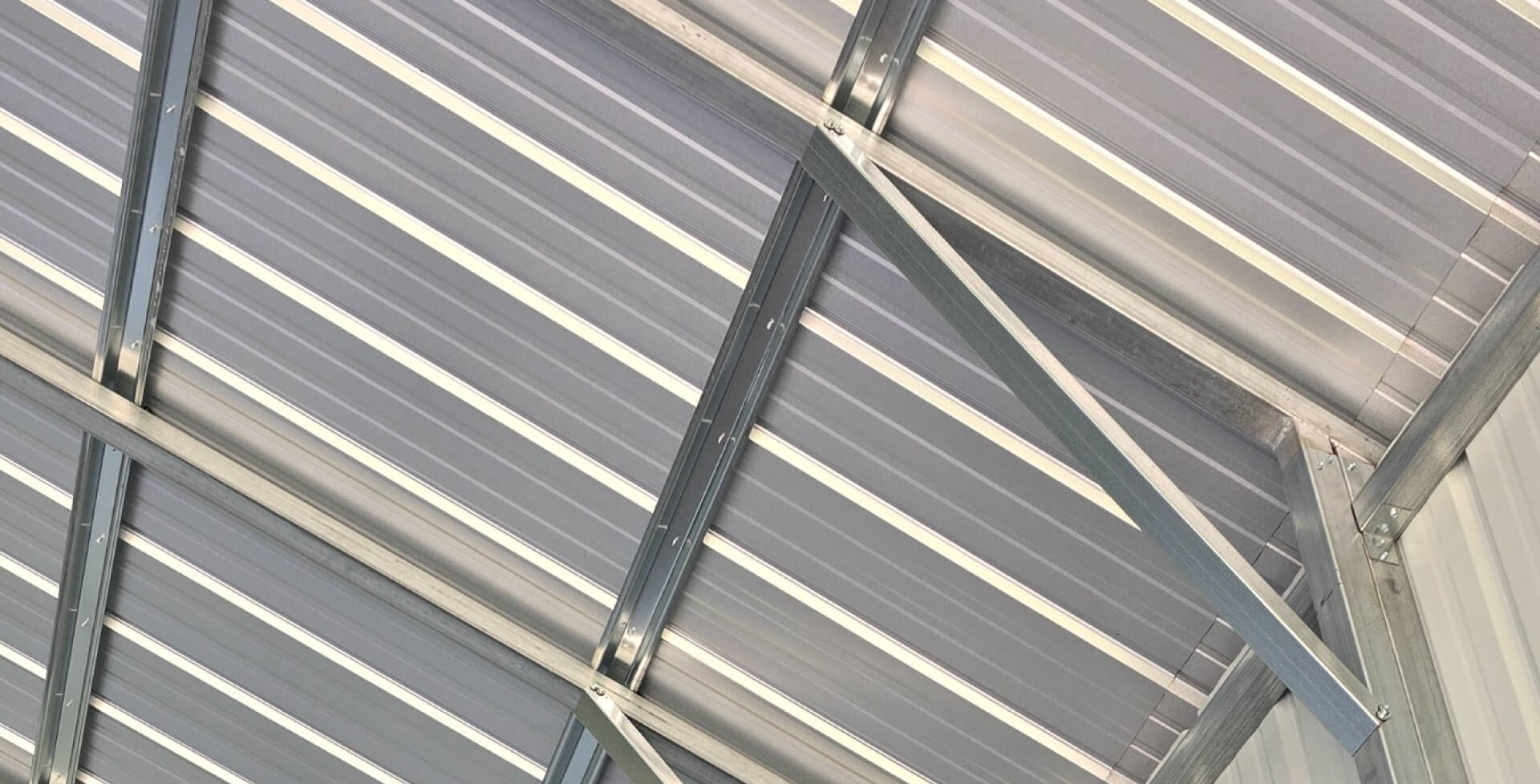 Close-up of corrugated metal roof panels and galvanized steel support beams inside a metal building, illustrating durable roof construction and structural design.