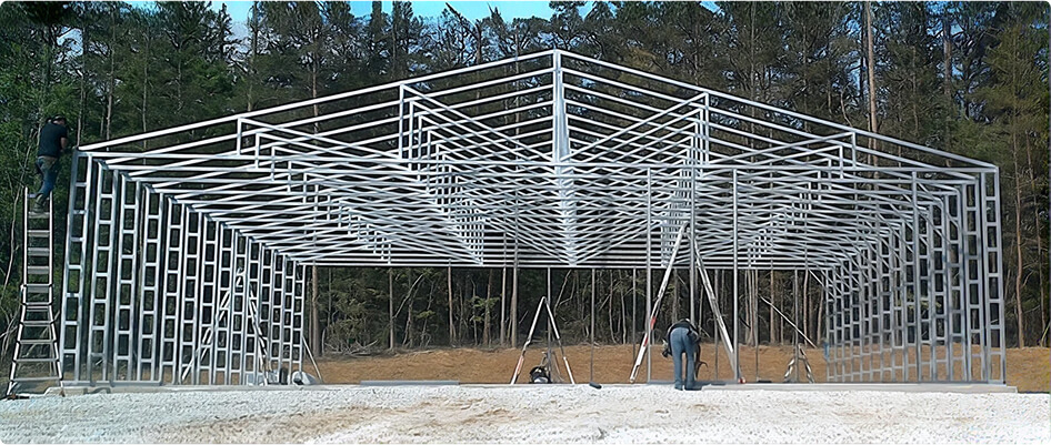 A worker erects the trusses of a 60-foot-wide metal building