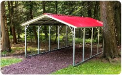 Open-sided metal carport with red roof providing covered vehicle or equipment storage in a wooded setting