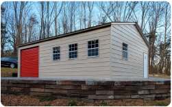 Residential-style metal garage with beige siding, red roll-up door, windows, and raised foundation