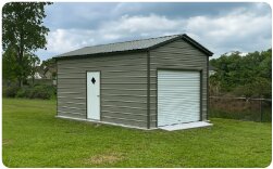 Compact gray metal garage with white roll-up door and side entry door on a residential property