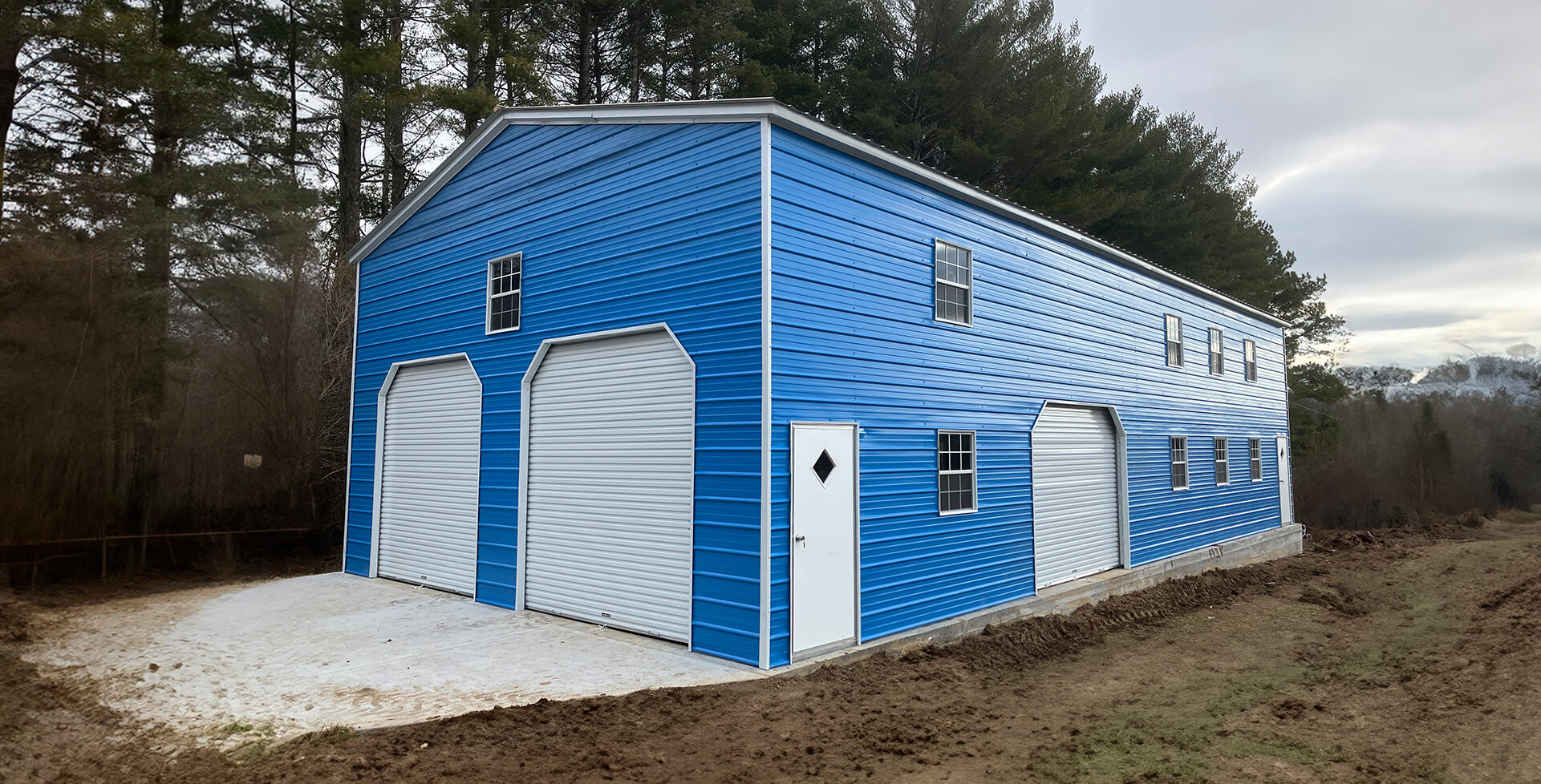 Large blue two-story metal garage with three white roll-up doors, multiple windows, and walk-in entry doors.