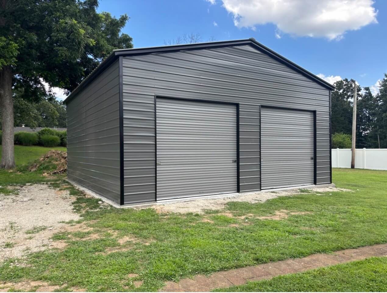 Gray metal garage with two large roll-up doors, black trim, gable roof, and horizontal metal siding.