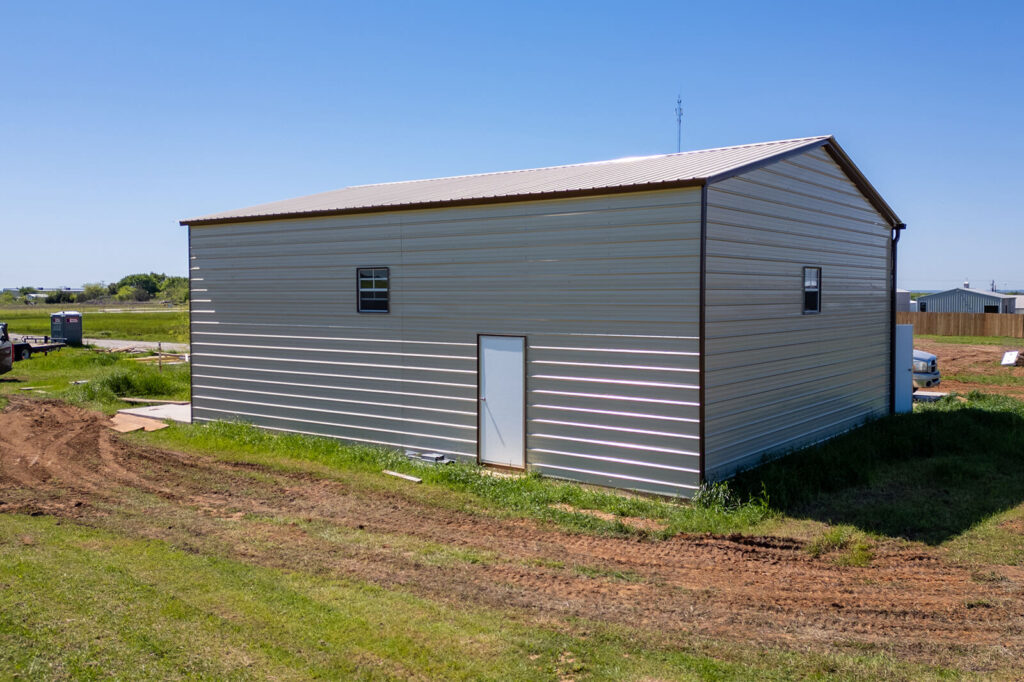 Large gray metal garage with a gable roof, upper-level windows, and a side walk-in door.