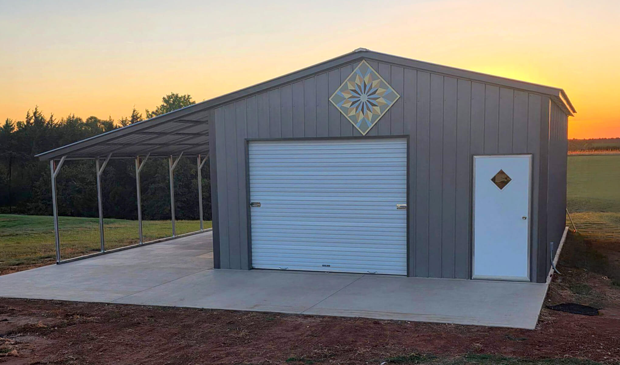 Gray metal garage with a white roll-up door, walk-in entry, and attached open-sided carport on a concrete slab.
