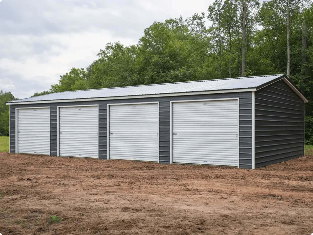A photo shows a long, single-story metal garage with four white roll-up doors on the front and dark gray siding. The building sits on a dirt lot with trees in the background.